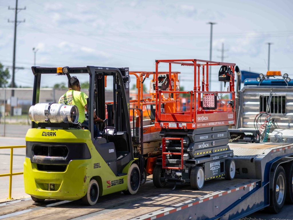 man driving rental forklift and scissor lifts onto a trailer at National Lift Truck